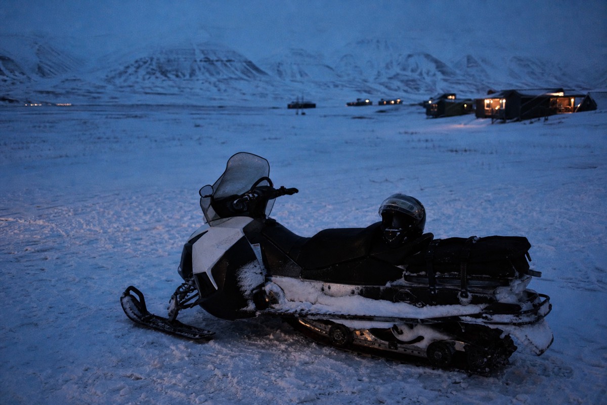 Line of snowmobiles crossing the wide white floor of Adventdalen under low winter light