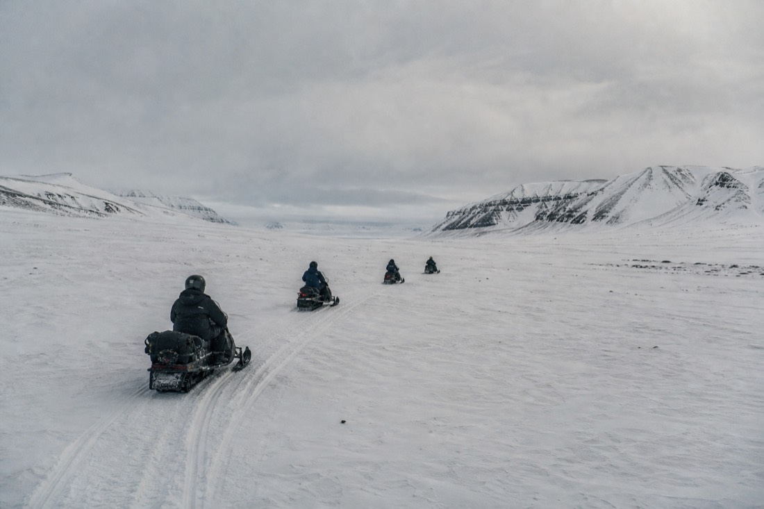 Line of snowmobiles crossing the wide white floor of Adventdalen on a Svalbard snowmobile tour